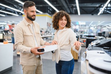 Genç çift yeni bir robot elektrik süpürgesi seçiyor. Elektronik mağazasında farklı modelleri karşılaştırıyorlar.