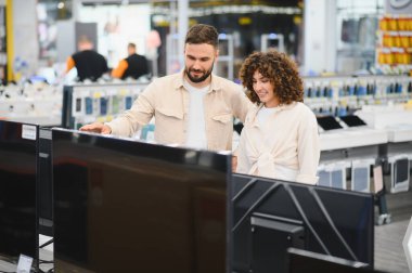 Genç çift elektronik mağazasından ev aletleri alırken modern televizyonu işaret ediyor