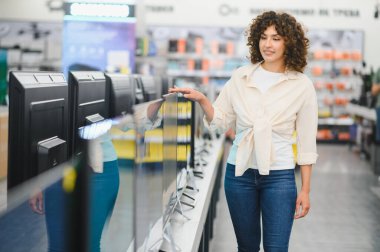 Modern televizyonları kıyaslayan, tüketici elektroniği mağazasında ev eğlencesi arayan genç bir kadın.