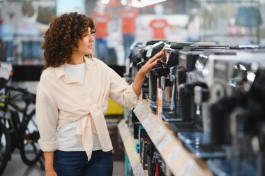 Müşteri bir ev aletleri dükkanından kahve makinesi seçiyor, satın almadan önce çeşitli modelleri inceliyor.
