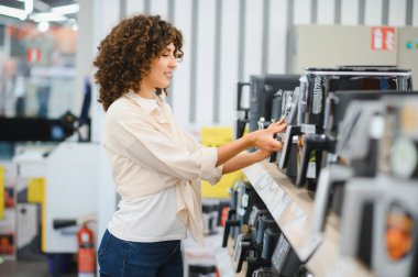 Müşteri, bir ev aletleri mağazasının raflarına bakarken yeni bir kahve makinesi seçiyor ve çeşitli seçenekleri faiziyle değerlendiriyor