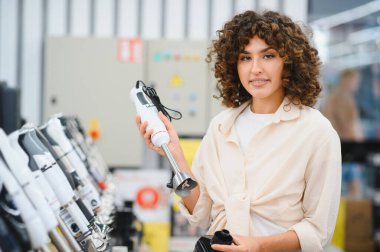 Müşteri farklı modellerdeki daldırma mikserlerini bir mağazada karşılaştırıyor, mutfak eşyaları için satın alma kararları alıyor.