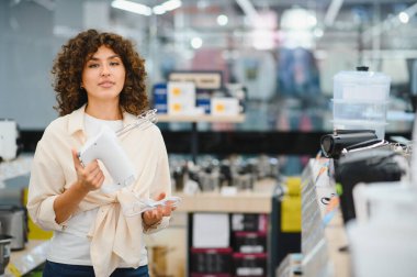Bir perakende mağazasından ev aletleri alırken elinde elektrikli mikser tutan müşteri mutfak ihtiyaçlarını değerlendiriyor.