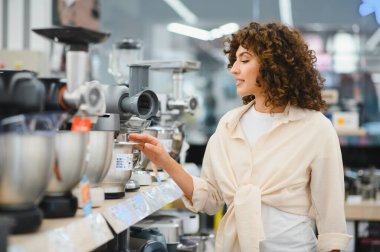 Bir ev aletleri mağazasında yiyecek işlemcisi seçen genç bir kadın vitrindeki çeşitli modelleri inceliyor.