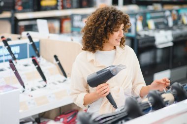 Perakende mağazasından ev aletleri alırken çeşitli saç kurutma makinelerini karşılaştıran müşteri, kişisel bakım gereksinimleri seçeneklerini değerlendiriyor
