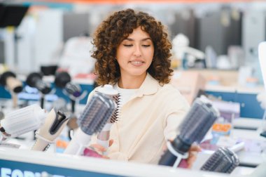 Müşteri, ev aletleri mağazasında dönen sıcak hava fırçalarını karşılaştırıyor, saç bakımı için satın alma kararı veriyor