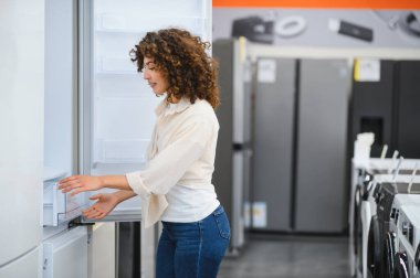 Ev aletleri mağazasında buzdolabı kapısı açan müşteri özelliklerini inceleyip satın alma kararı veriyor.