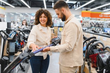 Mutlu çift yeni bir elektrikli süpürge seçiyor, elektronik mağazasında birlikte alışveriş yapıyorlar, evleri için satın alma kararı veriyorlar.