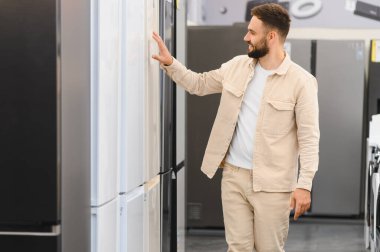 Gülümseyen müşteri yeni buzdolabını seçerken elektronik mağazasının canlı galerisinden ev aletleri alıyor.