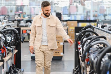 Gülümseyen bir müşteri yeni bir elektrikli süpürge seçerken alışveriş deneyiminin tadını çıkarıyor.