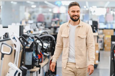 Ev aletleri mağazasında yeni bir elektrikli süpürge seçen mutlu adam, alışveriş deneyiminin tadını çıkarıyor.