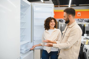 Bir çift, buzdolabının özelliklerini tartışarak bir elektronik mağazasında seçenekleri araştırıyor. Nişanlı gibiler ve satın almakla ilgileniyorlar.