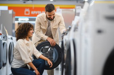 Mutlu çift, seçeneklerle dolu geniş bir ev aletleri mağazasında birlikte vakit geçirirken yeni bir çamaşır makinesi seçiyor.