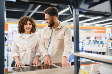 Mutlu çift ev aletleri mağazasında yeni bir indüksiyon sobası seçiyor, özellikleri tartışıyor ve satın alma kararı alıyorlar.