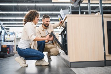 Ev aletleri mağazasında mutfak aletlerini karıştıran mutlu çift evleri için zarif ve modern bir fırını dikkatle inceliyor.