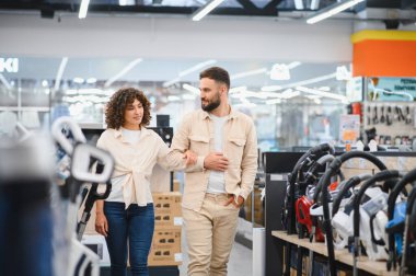 Bir çift elektronik mağazasına girip çeşitli ev aletlerini karıştırıyor. İhtiyaçları için en iyi seçenekleri seçmekle meşgul görünüyorlar.