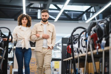 Genç çift bir ev aletleri dükkanına göz atıyorlar, birlikte alışveriş yaparken mükemmel bir elektrikli süpürge seçiyorlar.