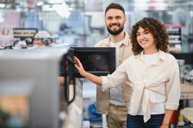 Mutlu çift yeni bir mikrodalga fırın seçerek ev aletleri mağazasında mutfak alışverişi yapıyor.