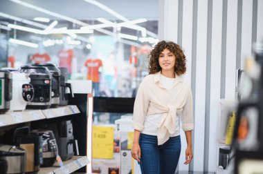 Genç bir kadın elektronik mağazasına girip modern ev ve yemek pişirme deneyimini geliştirmek için en son mutfak aletlerini arıyor.