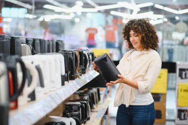 Elektronik mağazasında elektrikli su ısıtıcısını inceleyen müşteri mutfak ekipmanları için satın alma kararı veriyor.