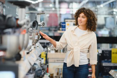 Ev aletleri mağazasında mutfak robotunu gösteren genç bir kadın yemek pişirmek için yeni bir alet arıyor.
