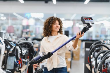 Müşteri ev aletleri mağazasında kablosuz elektrik süpürgesini inceliyor, ev temizliği için satın alma kararı veriyor.