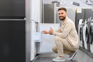 Bir mağazada yeni bir buzdolabı seçerken, alışveriş deneyiminin tadını çıkaran mutlu müşteri başparmağını kaldırıyor.