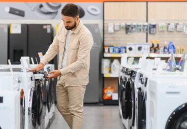 Alet mağazasından yeni çamaşır makinesi seçen, özelliklerini karşılaştıran ve satın alma kararı alan bir adam