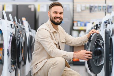 Gülümseyen müşteri bir elektronik mağazasında çamaşır makinesini kontrol ediyor, ev aletlerini seçiyor.