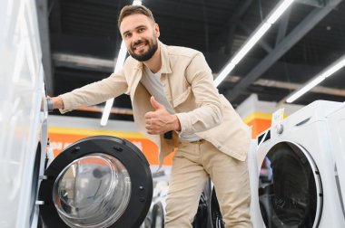 Elektronik mağazasında yeni bir çamaşır makinesi seçerken, alışveriş deneyiminin tadını çıkaran mutlu bir müşteri.