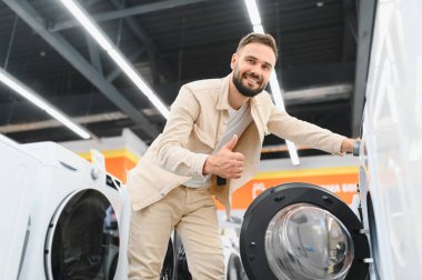 Neşeli bir ev aletleri mağazasında çamaşır makinesini seçerken, alışveriş deneyiminin tadını çıkaran mutlu bir müşteri.