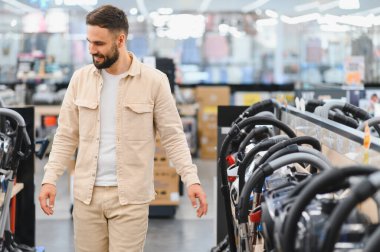 Gülümseyen müşteri çeşitli seçenekler ve görüntülerle dolu canlı bir ev aletleri mağazasında yürürken bir elektrik süpürgesi seçiyor.