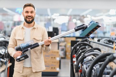 Elektronik mağazasında alışveriş yaparken elinde yeni bir kablosuz süpürge tutan mutlu müşteri, modern aletlerin seçiminin tadını çıkarıyor.