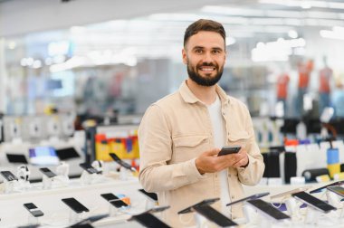 Gülümseyen müşteri akıllı telefonları karıştırırken bir elektronik mağazasında yeni bir cep telefonu aygıtı seçiyor, alışveriş deneyiminin tadını çıkarıyor