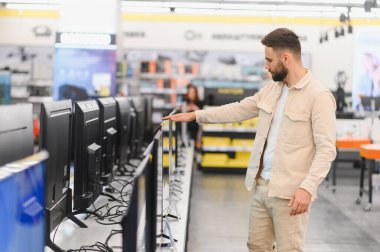 Tüketici elektroniği mağazasından yeni bir televizyon seçen sakallı adam, vitrindeki farklı modelleri karşılaştırıyor.