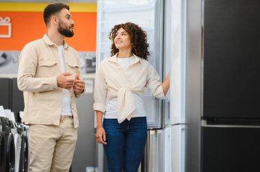 Mutlu çift elektronik mağazasında yeni buzdolabı seçiyor, özellikleri tartışıyor ve evleri için satın alma kararı veriyorlar.