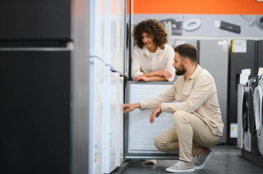 Mutlu çift elektronik mağazasından yeni buzdolabı seçiyor, ev aletlerini inceliyor, mutfak aletleri için alışveriş yapıyor.