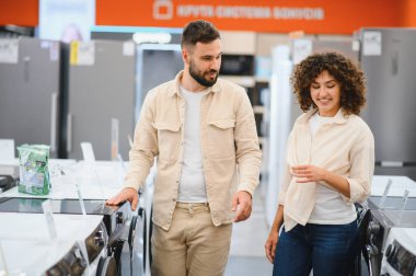 Mutlu çift yeni bir çamaşır makinesi alıyor. Parlak bir elektronik mağazasında birlikte seçim sürecinin tadını çıkarıyorlar.