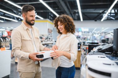 Robot elektrikli süpürge tutan mutlu çift elektronik mağazasından ev aletleri alıyor.