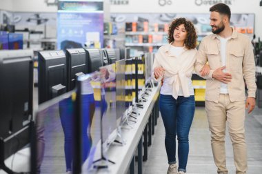 Çift, çeşitli ev aletleri arasında yeni bir televizyon seçeneklerini keşfetmek için bir elektronik mağazasına giriyor.