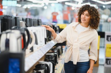 Müşteri bir ev aletleri mağazasında yeni bir elektrikli su ısıtıcısı seçiyor, görüntüdeki farklı modelleri karşılaştırıyor