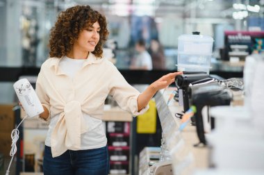 Bir perakende mağazasından ev aletleri alırken çeşitli mutfak mikserleri ve mikserlerini karşılaştıran müşteri, seçenekleri ve fiyatları değerlendiriyor