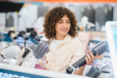 Müşteri bir elektronik mağazasında saç kurutma makinelerini karşılaştırıyor, mükemmel bir saç bakım aleti arıyor.