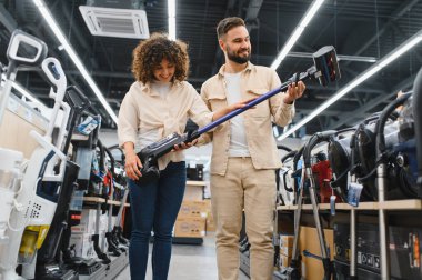 Modern ev aletleri mağazasında alışveriş yaparken yeni kablosuz elektrik süpürgesini inceleyen mutlu çift.