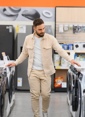 Müşteri çamaşır makinelerini karşılaştırıyor, elektronik mağazasında yürüyor, alışveriş yapmadan önce seçenekleri dikkatlice değerlendiriyor.