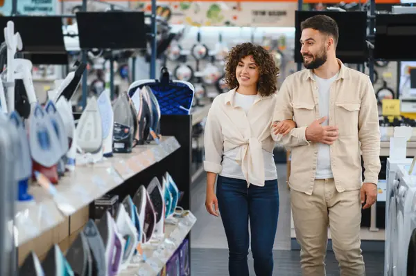 Elektronik mağazasında yürüyen mutlu çift yeni bir ütü, alışveriş ve tüketim konsepti seçiyor.