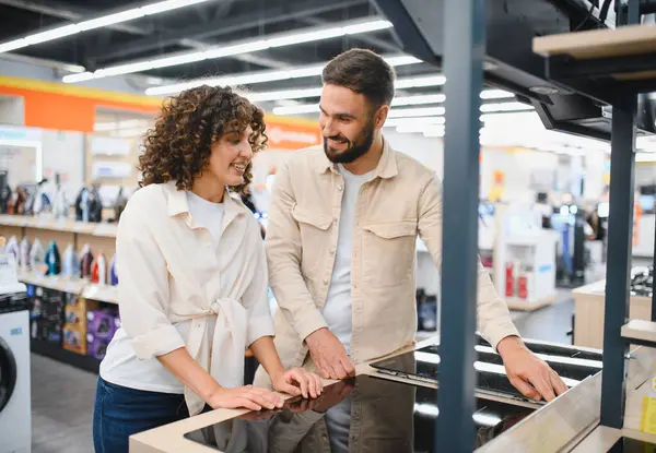 Mutlu çift modern indüksiyon sobası seçiyor, elektronik mağazasında yeni ev aletleri alışverişinin keyfini çıkarıyorlar.