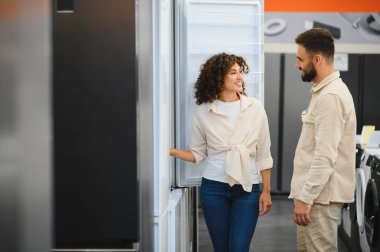 Mutlu çift elektronik mağazasında yeni buzdolabı seçiyor, özellikleri tartışıyor ve evleri için satın alma kararı veriyorlar.