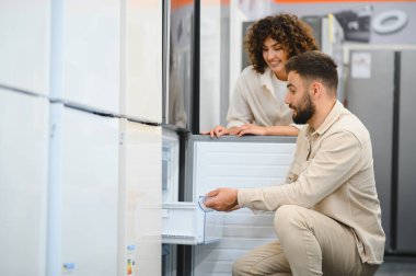 Bir elektronik mağazasında çeşitli buzdolabını karıştıran mutlu çift, evleri için mükemmel aletleri seçme sürecinin tadını çıkarıyor.