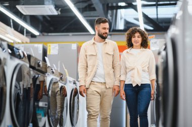 Bir çiftin elektronik mağazasında çamaşır makinelerini karıştırıp ev aletlerinin ihtiyaçlarını değerlendirmeleri.